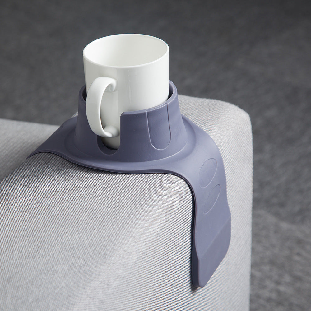 Silicone cup holder draped over a couch armrest with a drink in it